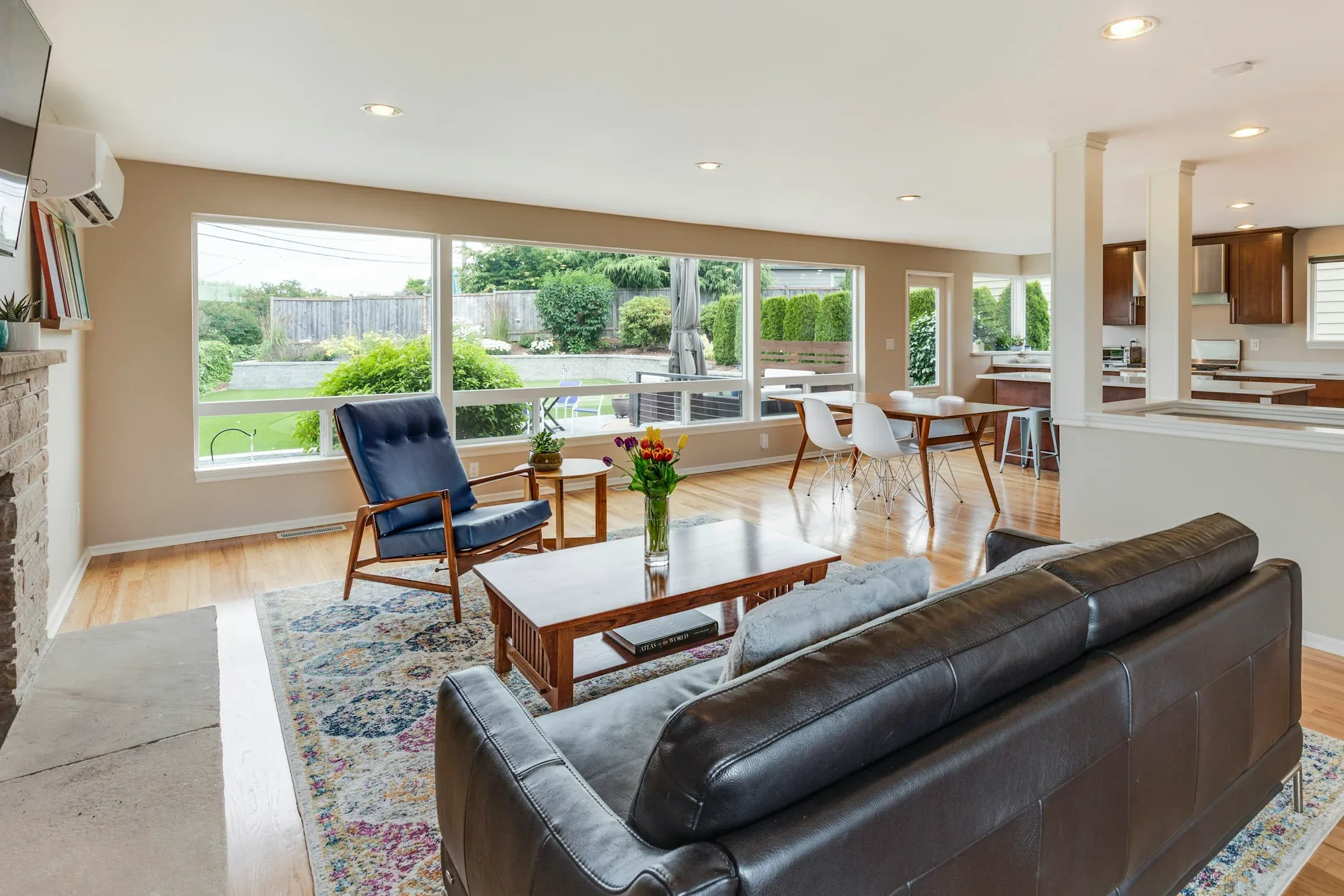 A bright open living room with wood flooring, leather seating, and wide garden windows