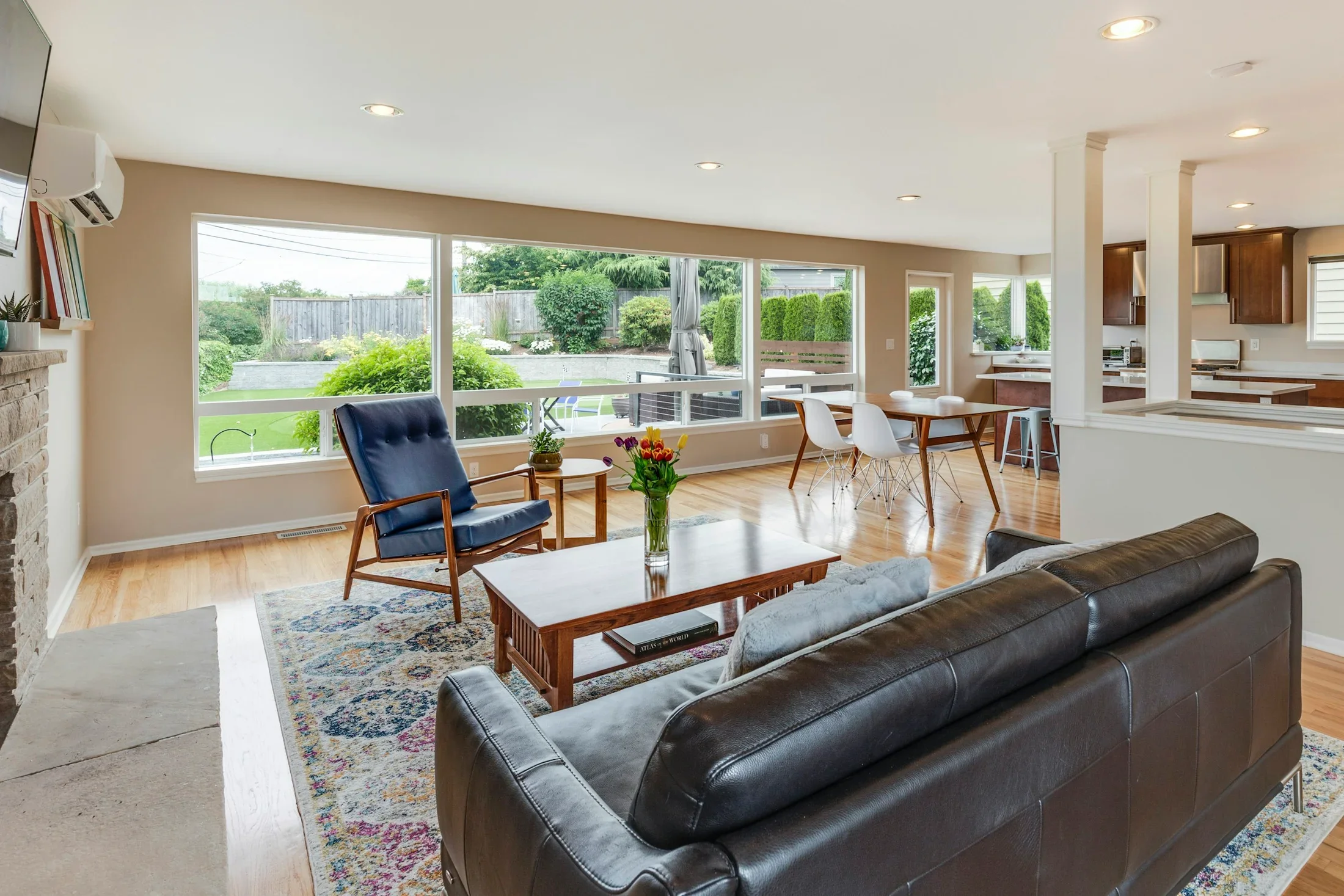 A bright open living room with wood flooring, leather seating, and wide garden windows