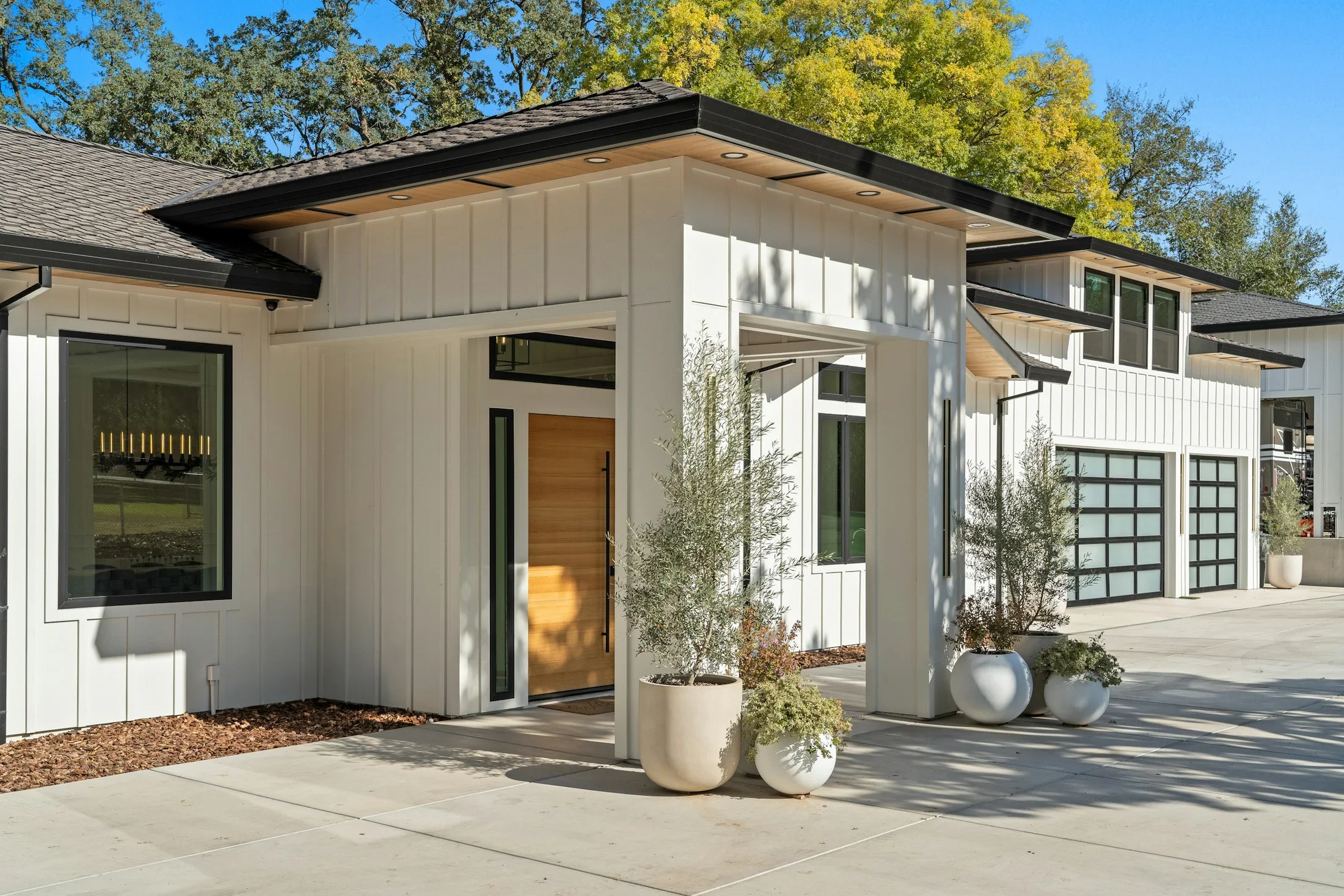 A white farmhouse-style home with a wood front door and landscaped entry