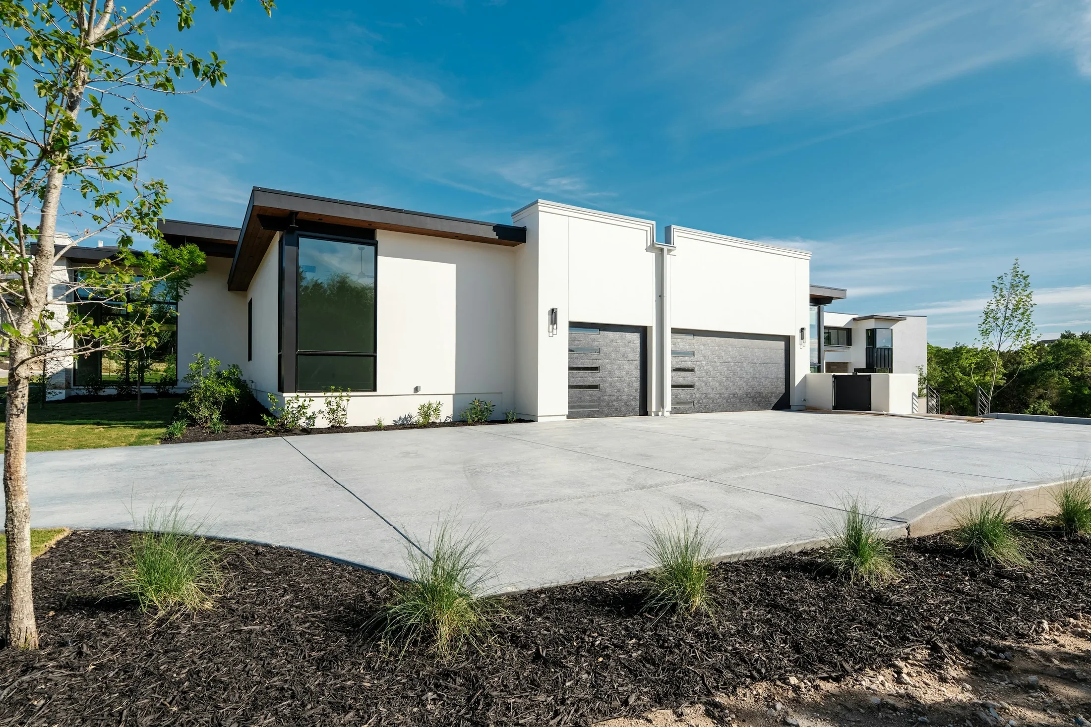 A contemporary white home with a broad driveway, garage doors, and young trees