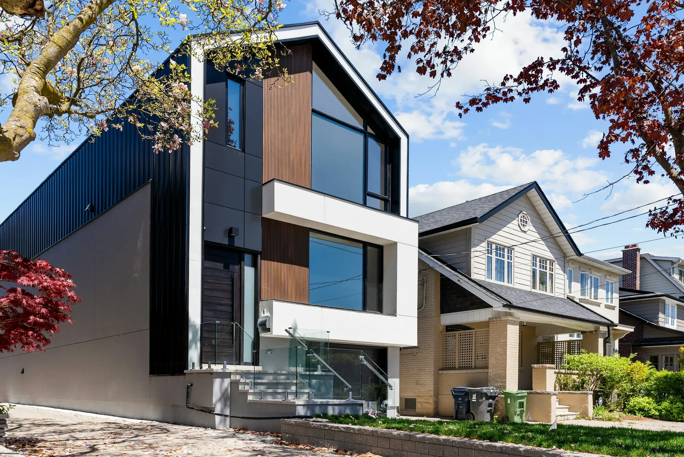 A modern dark-clad home beside a traditional house on a residential street